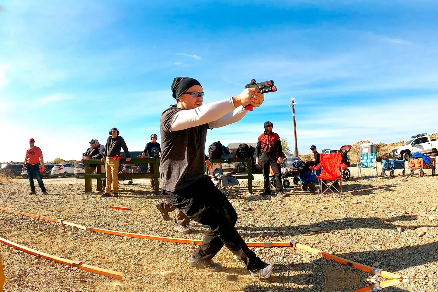 Man firing a revolver while crouching outdoors.